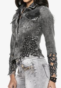 Harmaa farkkutakki, jossa kulutettuja yksityiskohtia, mustat pitsikoristeet helmassa ja hihoissa sekä helmi- ja paljettikoristeita.