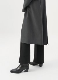 Μαύρες τακούνες μπότες αστραγάλου με μυτερή μύτη, υφή, συνδυασμένες με κομμένα γκρι παντελόνια και ένα αντίστοιχο μακρύ παλτό.