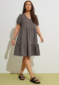 Vestido gris de capas con escote en V, mangas cortas abullonadas y tela texturizada. Combinado con sandalias negras con lunares blancos.