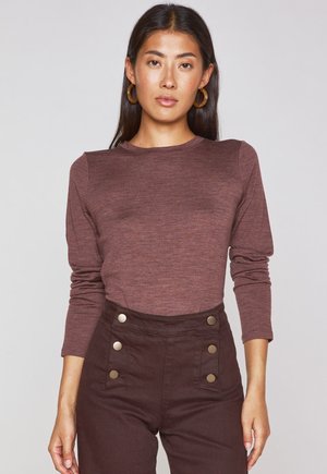 Long-sleeve, fitted top in a maroon textured fabric, paired with high-waisted brown pants featuring metallic button accents.