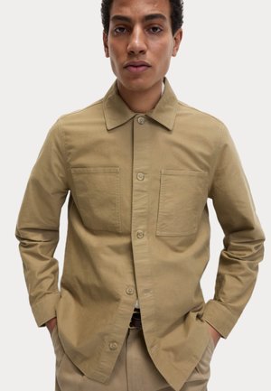 Camisa beige con cuello, dos bolsillos en el pecho y mangas largas. Está hecha de una suave tela de mezcla de algodón.