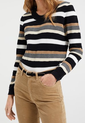 Striped knit sweater featuring black, white, beige, and tan horizontal stripes; ribbed texture; round neck; paired with tan corduroy pants.