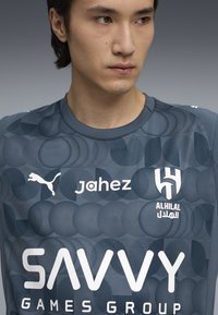 Jersey atlético de color gris oscuro con un patrón circular, con logotipos blancos de Puma, Jahez y Al Hilal. Cuello redondo y tejido texturizado.