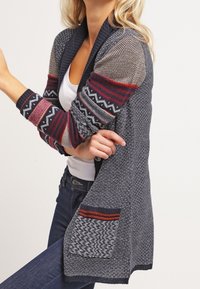 Sweter kardigan w kolorze granatowym z wzorzystymi rękawami w czerwonym i szarym kolorze, z kołnierzem szalowym oraz teksturowaną kieszenią z kontrastowymi paskami.