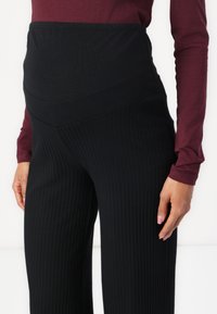 Pantalones de maternidad negros acanalados con una cintura ancha y suave. Combinados con un top ajustado de manga larga color granate; la tela parece suave y elástica.
