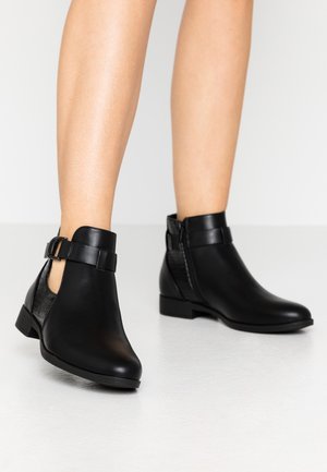 Bottines en cuir noir avec un talon plat, une fermeture éclair sur le côté et une sangle décorative avec une boucle. Texture lisse avec une finition mate.