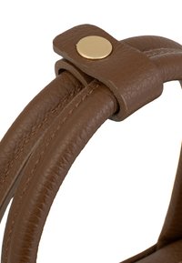Manico di una borsa in pelle marrone con una texture liscia, dettagli cuciti e un pulsante a scatto in metallo color oro rotondo.