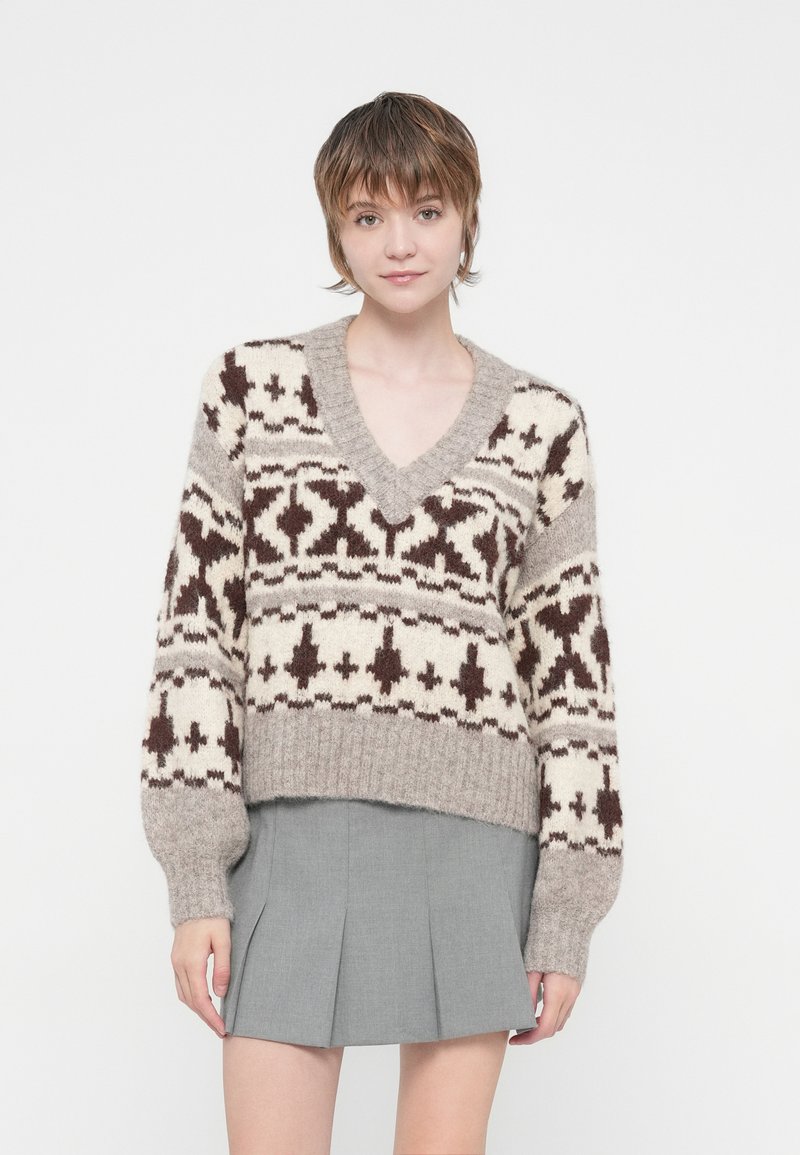Pull en tricot crème et marron avec un col en V, présentant un motif géométrique. Design court et ourlet côtelé, associé à une jupe plissée grise.