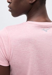 Κοντινό πλάνο ενός ατόμου που φοράει ένα ανοιχτό ροζ μακρυμάνικο μπλουζάκι με μικρό γκρι λογότυπο στο πάνω μέρος της πλάτης κοντά στη γραμμή του λαιμού.