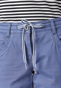 Light blue trousers with a drawstring waistband, featuring a silver button, pockets, and a smooth fabric texture. Striped top partially visible.