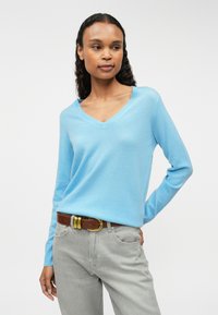 Világoskék V-nyakú pulóver, puha anyagból készült, hosszú ujjú, laza fazonú, szürke farmernadrággal és barna övvel párosítva.