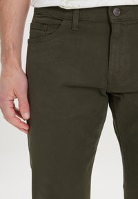 Donkergroene broek met een gladde textuur, voorzien van voorzakken, riemlussen en een enkele knoopsluiting op de taille.