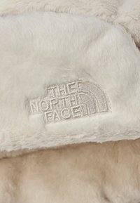 Kremowy, miękki polar z wyszywanym logo "The North Face" w jasnym kolorze na teksturowanej powierzchni.