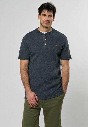 Marineblauwe, textuurgeefende polo met korte mouwen, voorzien van een placket met drie knopen en een embleem op de borst, gecombineerd met olijfgroene cargoshorts.