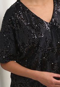 Black, sequined top with a V-neckline; features shimmering sequins on a soft fabric; loose, relaxed fit with short sleeves.