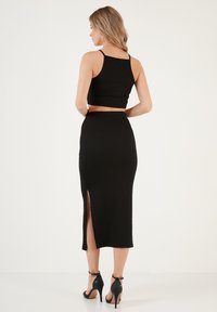 Haut noir court à fines bretelles associé à une jupe noire taille haute avec une fente sur le côté, porté avec des chaussures à talons hauts noires.