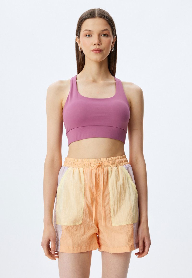 Sujetador deportivo morado cortado y pantalones cortos melocotón con bolsillos amarillos y lavanda. Los pantalones cortos tienen una cintura elástica y un detalle de cordón.