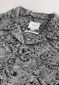 Camicia a fantasia paisley in bianco e nero, con vestibilità comoda, colletto, due bottoni neri e etichetta in tessuto con la scritta "NEXT".