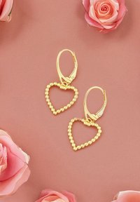 Guldörhängen i hartsform med ett pärlade design och lås som fästs på baksidan, visade mot en rosa bakgrund med rosor.
