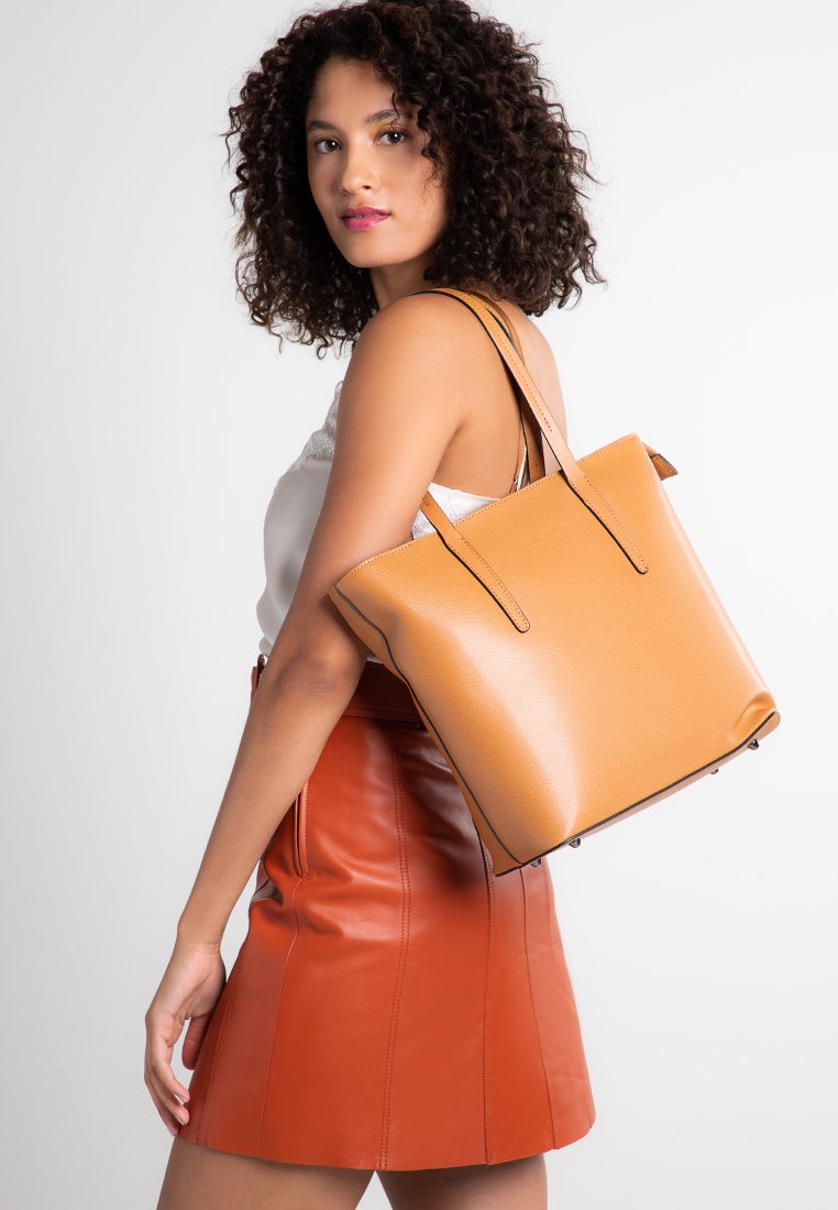 Borsa tote in pelle tan con due manici lunghi, forma strutturata e superficie testurizzata. Presenta cuciture a contrasto e piedini in metallo sul fondo.