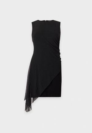 Une femme porte une robe noire asymétrique avec un pan drapé en tissu transparent, un sac à bandoulière bordeaux et des sandales à talons.