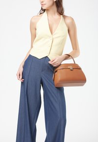 Borsa a tracolla in pelle color tan con forma strutturata e hardware dorato, abbinata a una top giallo a halter e pantaloni larghi blu navy.