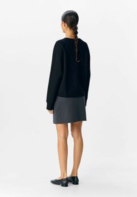 Sort sweatshirt, grå nederdel, flade sorte sko. Sweatshirten har rund halsudskæring, lange ærmer og en løs pasform. Glat tekstur.