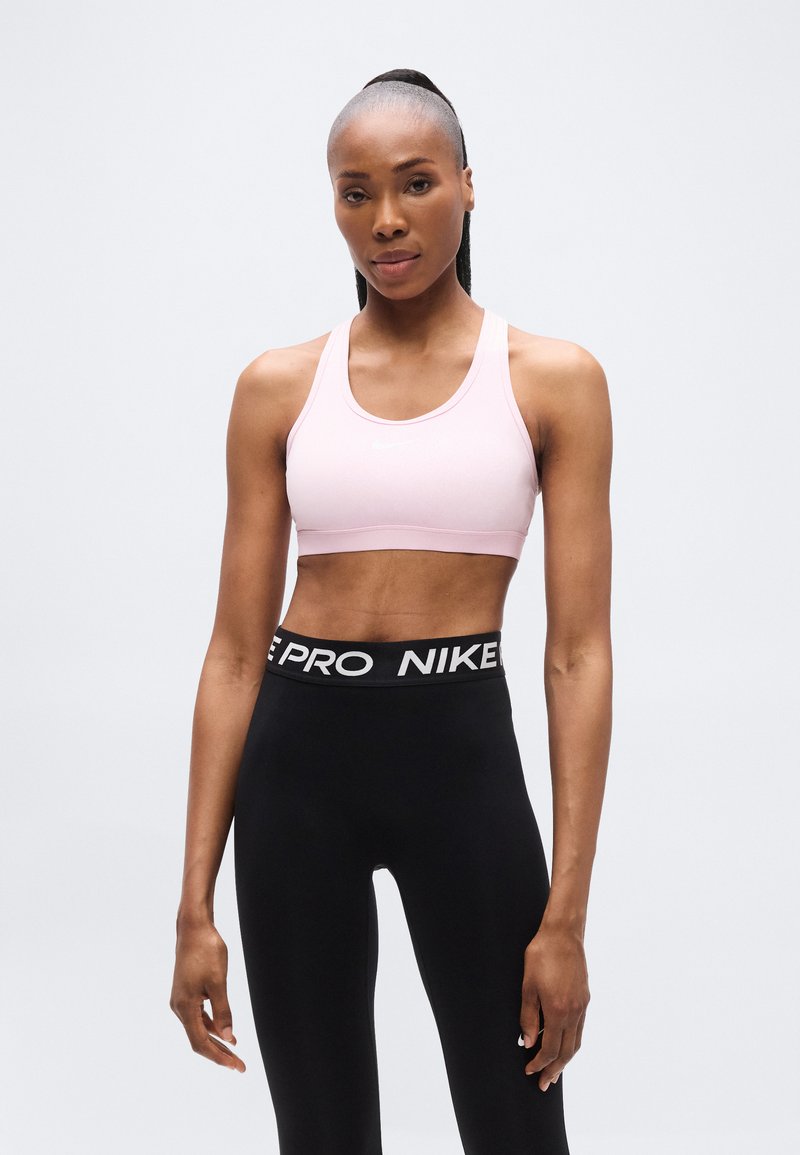 Ανοιχτό ροζ αθλητικό σουτιέν με λεία υφή και φαρδιές τιράντες, συνδυασμένο με μαύρο κολάν ψηλόμεσο με λευκή λωρίδα μέσης με λογότυπο.