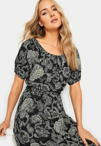 Schwarzes Kleid mit weißem Paisleymuster, kurzen Puffärmeln, elastischem Taillenbund und rundem Ausschnitt. Weicher Stoff mit fließendem Design.