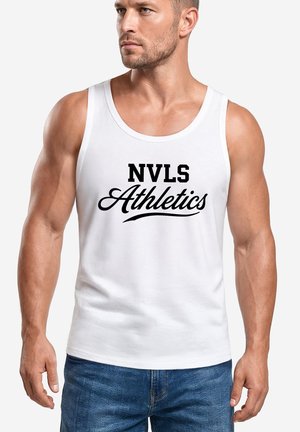 Muscular man wearing a white tank top with "NVLS Athletics" text printed in black, paired with blue jeans, standing against a plain background.