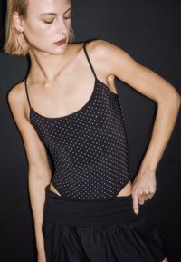 Czarny body z srebrnymi ćwiekami, wąskimi ramiączkami i niskim zapięciem na plecach. Połączone z czarną spódnicą z miękką, marszczoną talią.