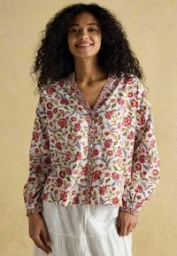 Bawełniana bluzka w kwiatowy wzór z długimi rękawami, z przodu na guziki, z dekoltem w kształcie litery V. Kolory to biały, czerwony, zielony i niebieski.