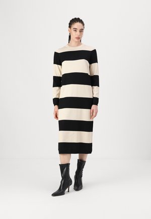 Striped dress in black and cream, with long sleeves and a relaxed fit. The model wears black ankle boots. Smooth fabric texture.