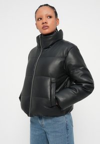 Černá pufová bunda z umělé kůže s vysokým límcem, zipem vpředu a dvěma bočními kapsami, s boxovým střihem a prošívaným designem.