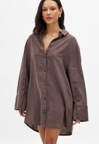 Abito camicia in lino marrone con vestibilità rilassata, maniche lunghe, chiusura frontale a bottoni e orlo arrotondato. Tessuto texturizzato.