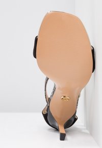 Chaussure à talons hauts avec une tige en daim noir, un talon à motif imprimé serpent et une semelle beige avec un accent doré sur le talon.