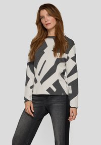 Grau-weiß gemusterter Pullover mit langen Ärmeln und Rundhalsausschnitt, gefertigt aus einem weichen Stoff. Kombiniert mit dunkelgrauen Jeans.