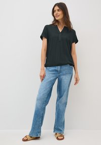 Blouse noire à col en V et à manches courtes, associée à un jean taille haute bleu clair et des sandales plates en osier. Design minimaliste et coupe décontractée.