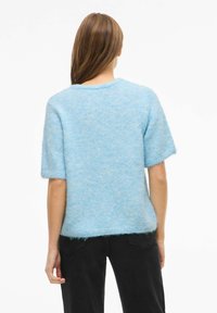 Lyseblå genser med kort erme laget av mykt, lodden materiale. Har rund hals og en litt løs passform, med uforsømte kantkanter.