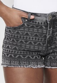 Melna un pelēka rakstaina džinsu šorti ar nolobītu apakšu, piedāvājot ģeometriskus dizainus, priekšējās kabatas un metāla pogu aizdari.