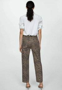 Pantalon imprimé léopard en beige et noir, doté d'une coupe droite et d'une taille haute. Le modèle porte une chemise de couleur claire.