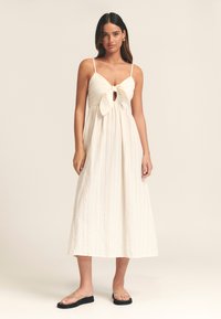 Kreemikas midi-kleit sõlmitava eesdetaili, kogutud büstiosa ja reguleeritavate rihmadega. Tekstuuriga kangas vertikaalsete triipudega.