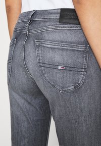 Jeans de mezclilla gris ajustados, con dos bolsillos traseros, un parche con logotipo en la cintura y sutiles detalles de desgaste.
