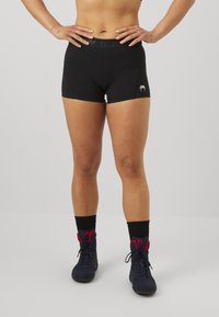 Μαύρα αθλητικά σορτς με εφαρμοστή σχεδίαση, μαλακή υφή και ζώνη μέσης με λογότυπο. Φορεμένα με ναυτικές αθλητικές παπούτσια και μαύρες κάλτσες.