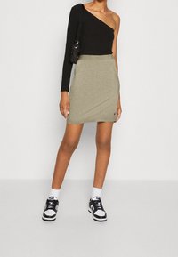 Czarny, żeberkowany top na jedno ramię w zestawieniu z dopasowaną, oliwkową spódnicą, noszony z czarno-białymi trampkami oraz małą czarną torebką.