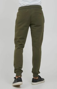 Zelene trenirke izrađene od mekanog materijala, s tapered dizajnom, rebrastim manžetama i stražnjim džepom s malim logotipom.