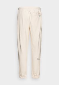 Pantalon jogger couleur crème en tissu doux, doté d'une taille élastique, de chevilles resserrées et de texte brodé sur la jambe.