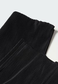 Tissu noir côtelé plié pour montrer une texture verticale et un tombé doux sur un fond clair.