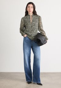 Bluză cu model floral, neagră și crem, cu mâneci lungi și o fundă la gât, purtată cu blugi evazați de culoare albastru deschis și o geantă neagră.