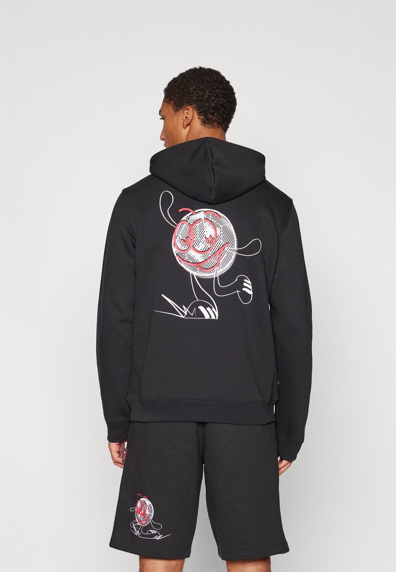 Svart hoodie i sweatshirtmaterial med en grafisk design av en leende tecknad karaktär i rött och vitt på ryggen.
